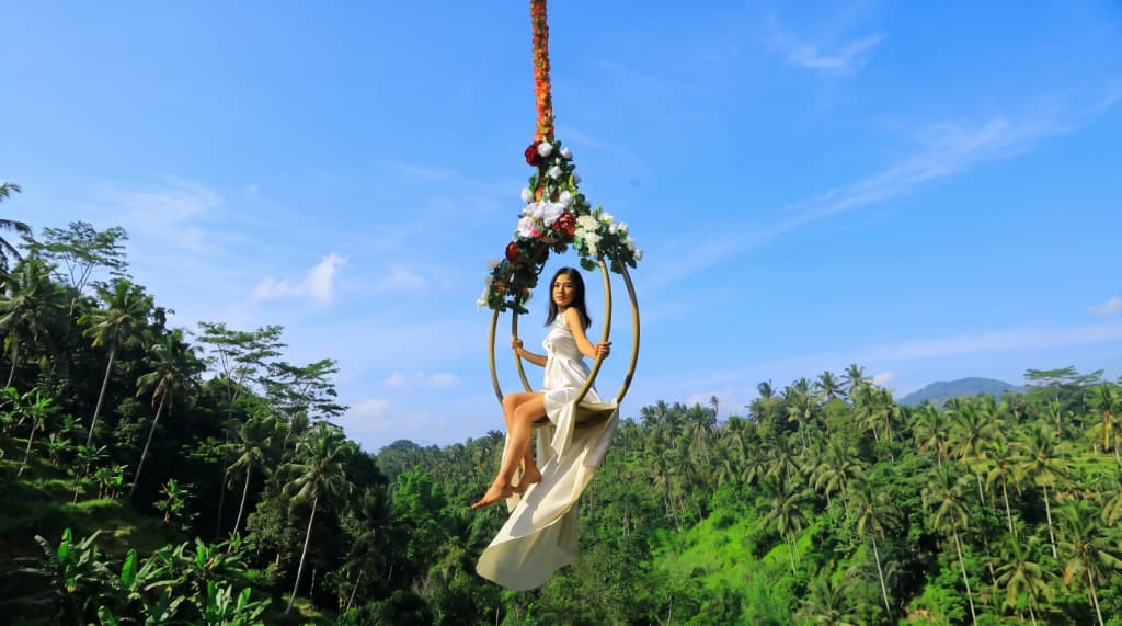 Guest in a white dress on the flower-draped hoop swing at Aloha Ubud Swing