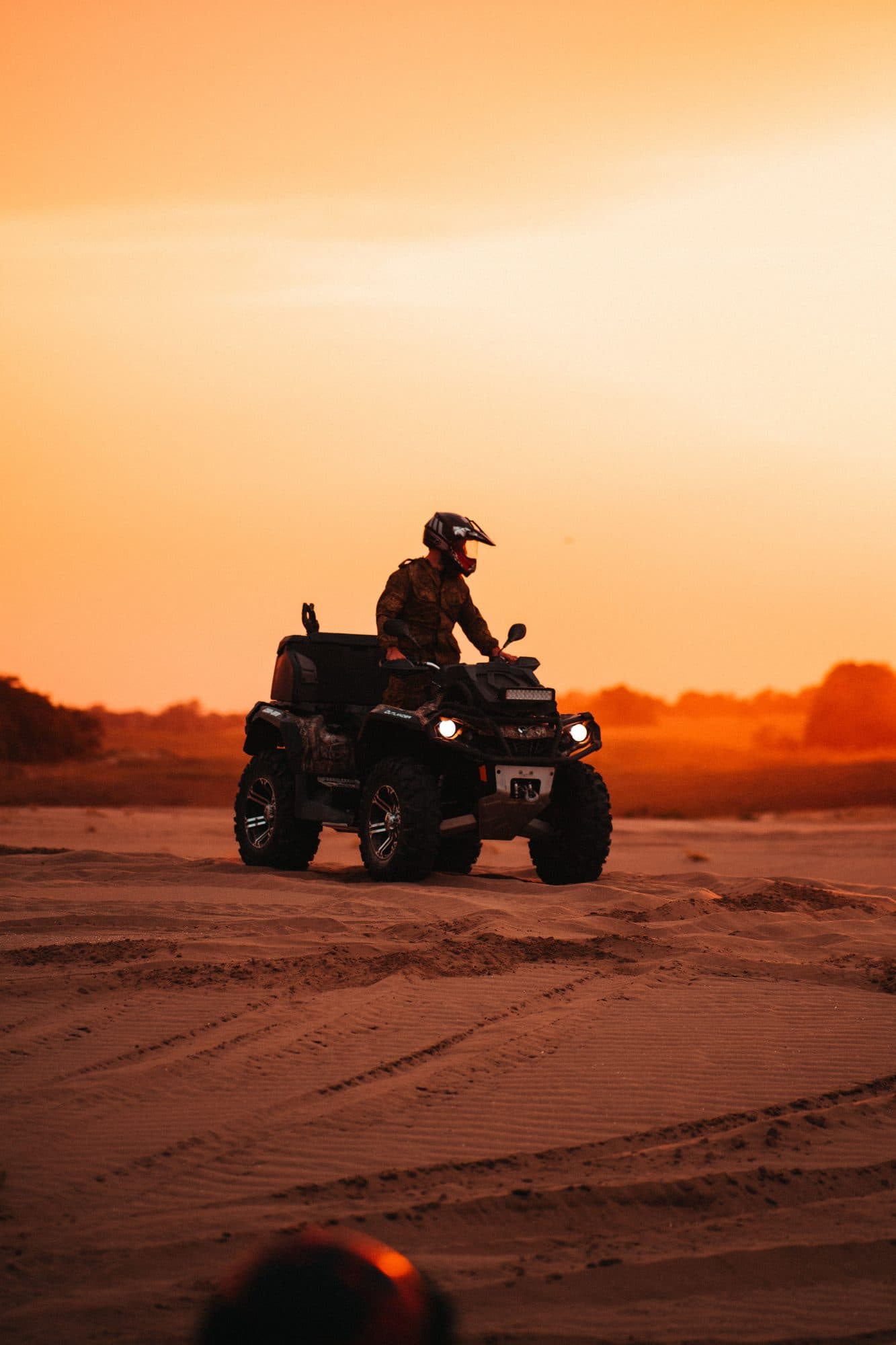 Rider in a helmet on a quad at sunset, headlights on