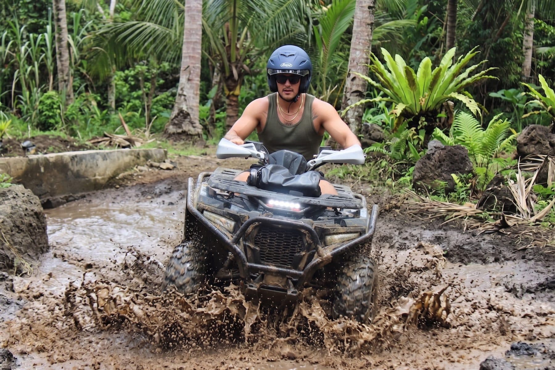 Rider in a helmet driving a quad through jungle mud on the Sedang ATV track