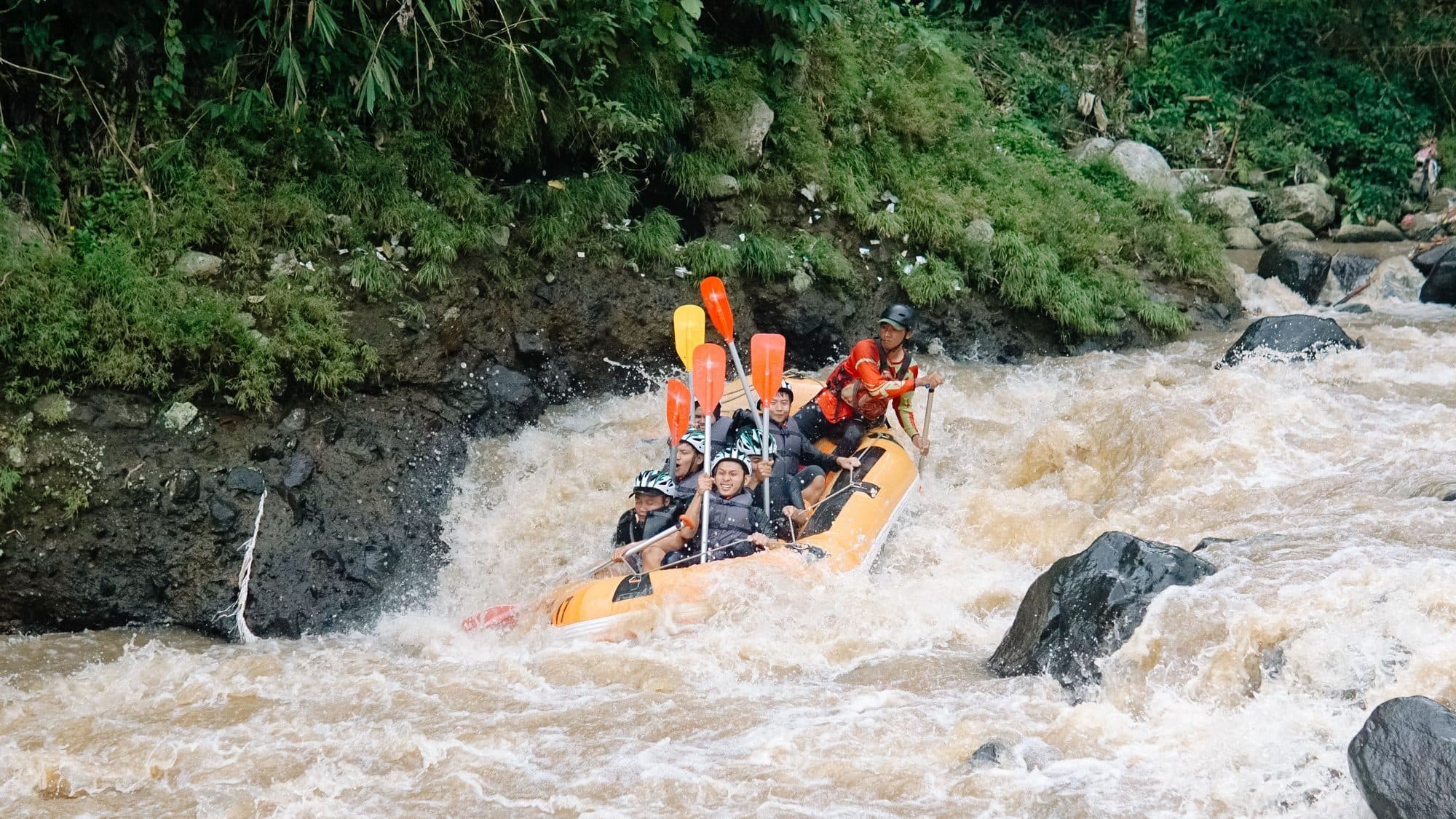An orange raft with a guide and guests paddling through whitewater on the Ayung