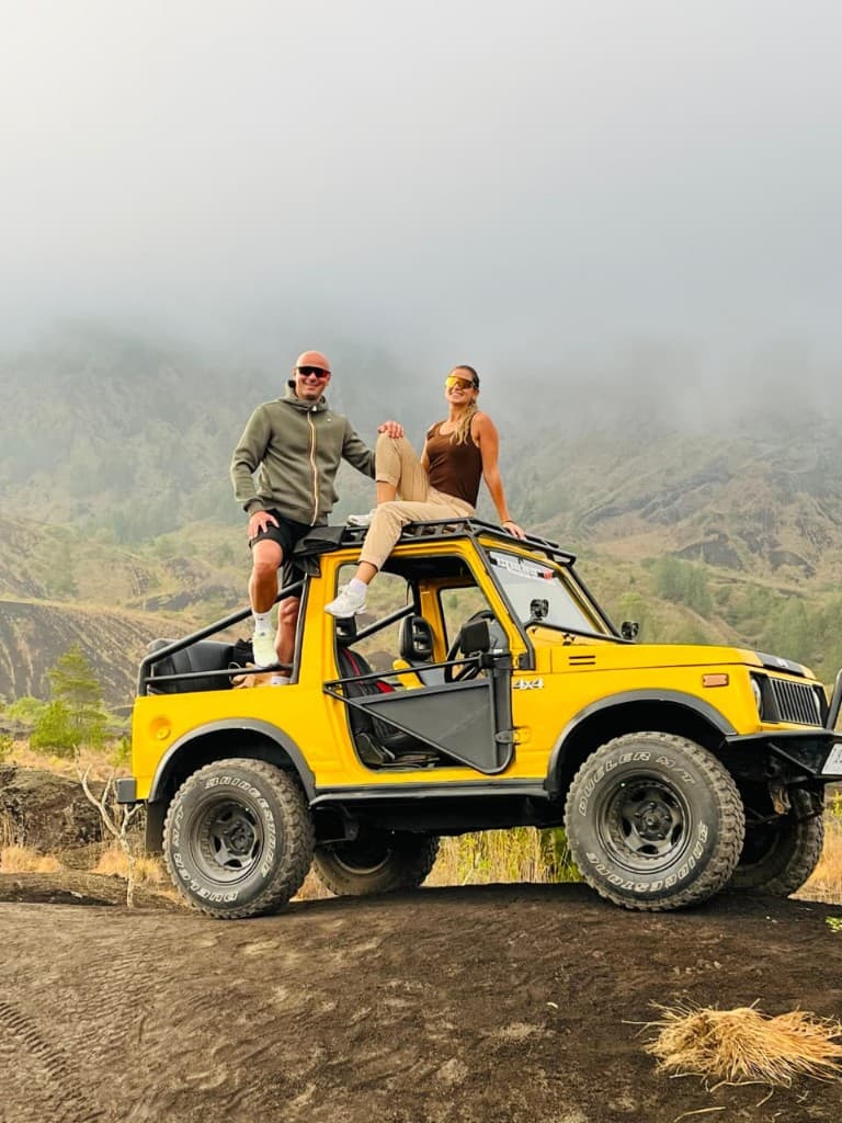 Two guests on an open yellow 4×4 under low cloud on a Mount Batur slope