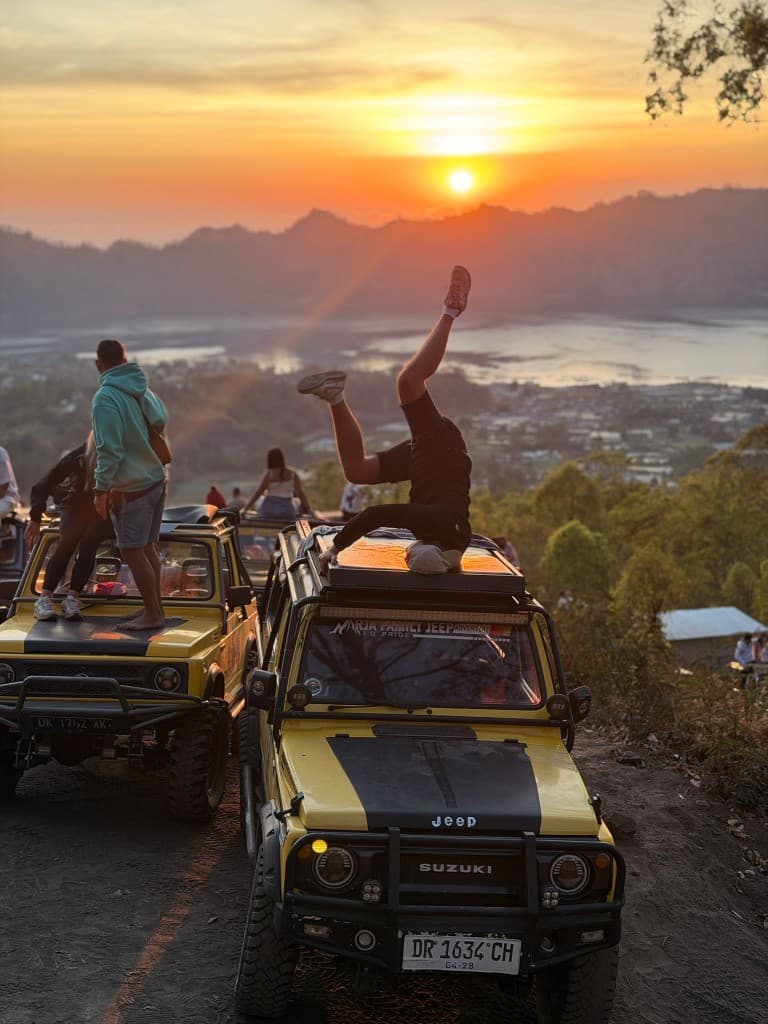 A guest doing a headstand on the roof of a yellow Suzuki jeep at sunrise above Lake Batur