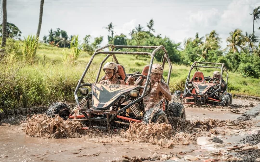 Two open off-road buggies on a muddy track, driver and passenger in the lead rig