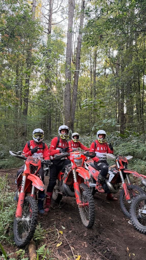 Four riders in red gear on orange dirt bikes among tall trees in the Kintamani forest