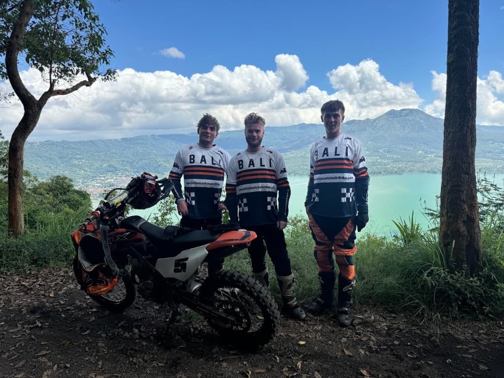 Three riders beside an orange KTM dirt bike on a ridge above Lake Batur