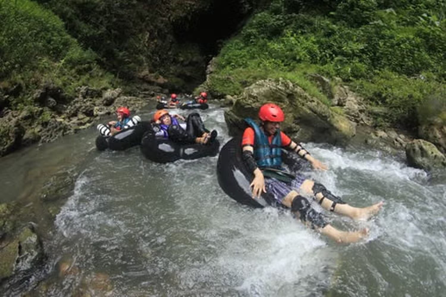 Riders in helmets and life jackets on sit-on tubes in a rocky river